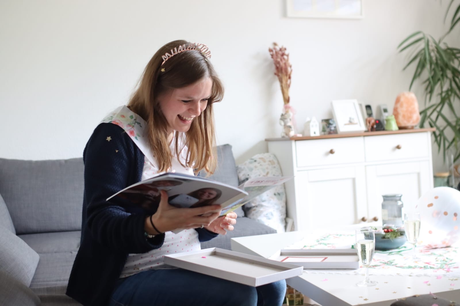 Eine werdende Mama strahlt vor Freude, während sie ihr persönliches Geschenk zur Baby-Party öffnet – ein liebevoll gestaltetes Magazin mit Erinnerungen, Glückwünschen und einem einzigartigen Podcast von Mitten ins Herz. Freunde und Familie haben ihre Stimmen und Wünsche für die Zukunft des Babys in einem emotionalen Audio-Geschenk verewigt. Ein bewegender Moment voller Überraschung, Liebe und unvergesslicher Erinnerungen.